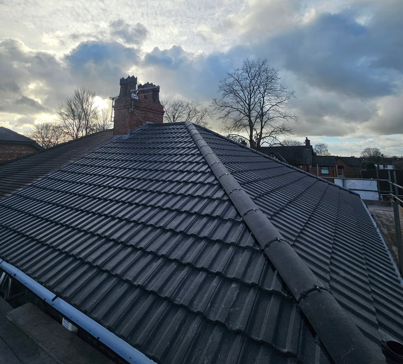 The same tiled roof after repair, clean and dark grey with a neat ridge and brick chimney